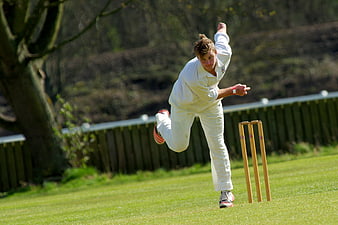 Cricket bowler in white uniform delivering ball on green field