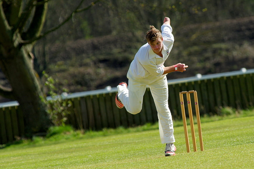 Cricket bowler in white uniform delivering ball on green field