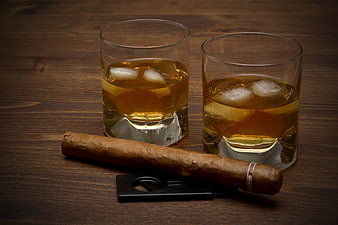 Two glasses of whiskey with ice and a cigar on wood