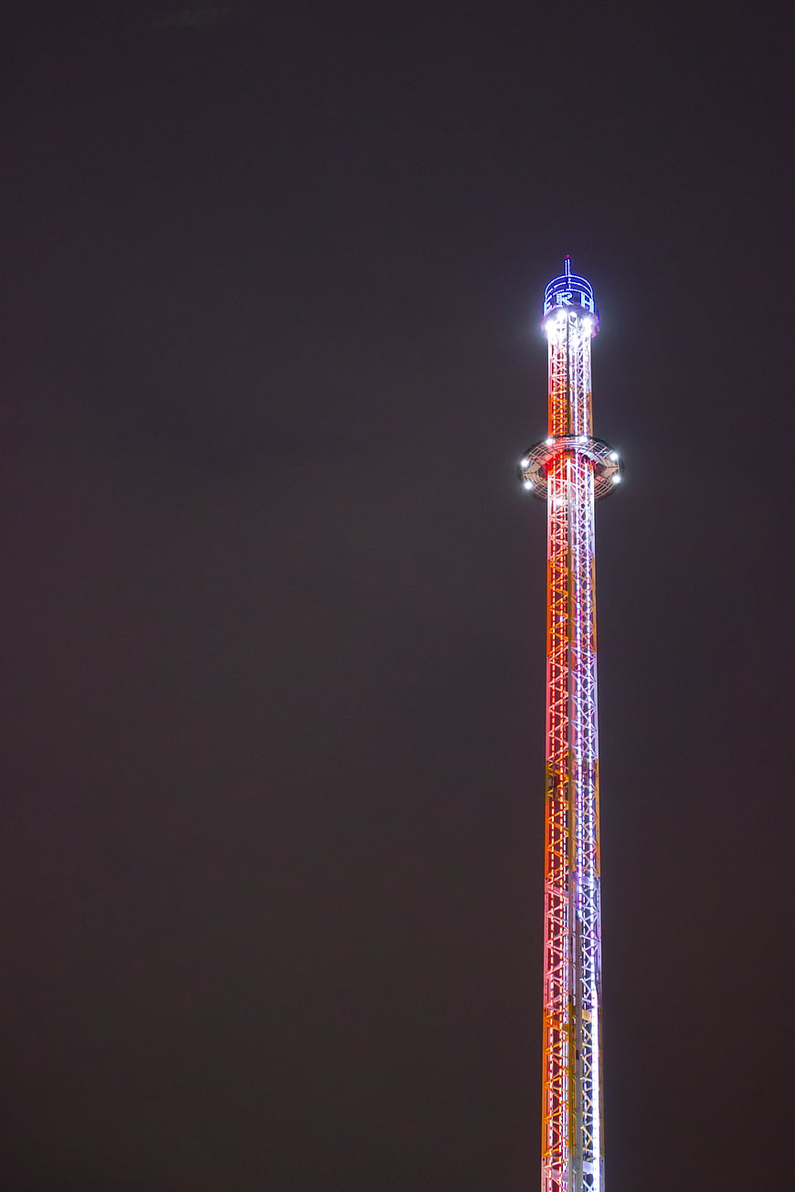 Illuminated funfair drop tower against dark night sky