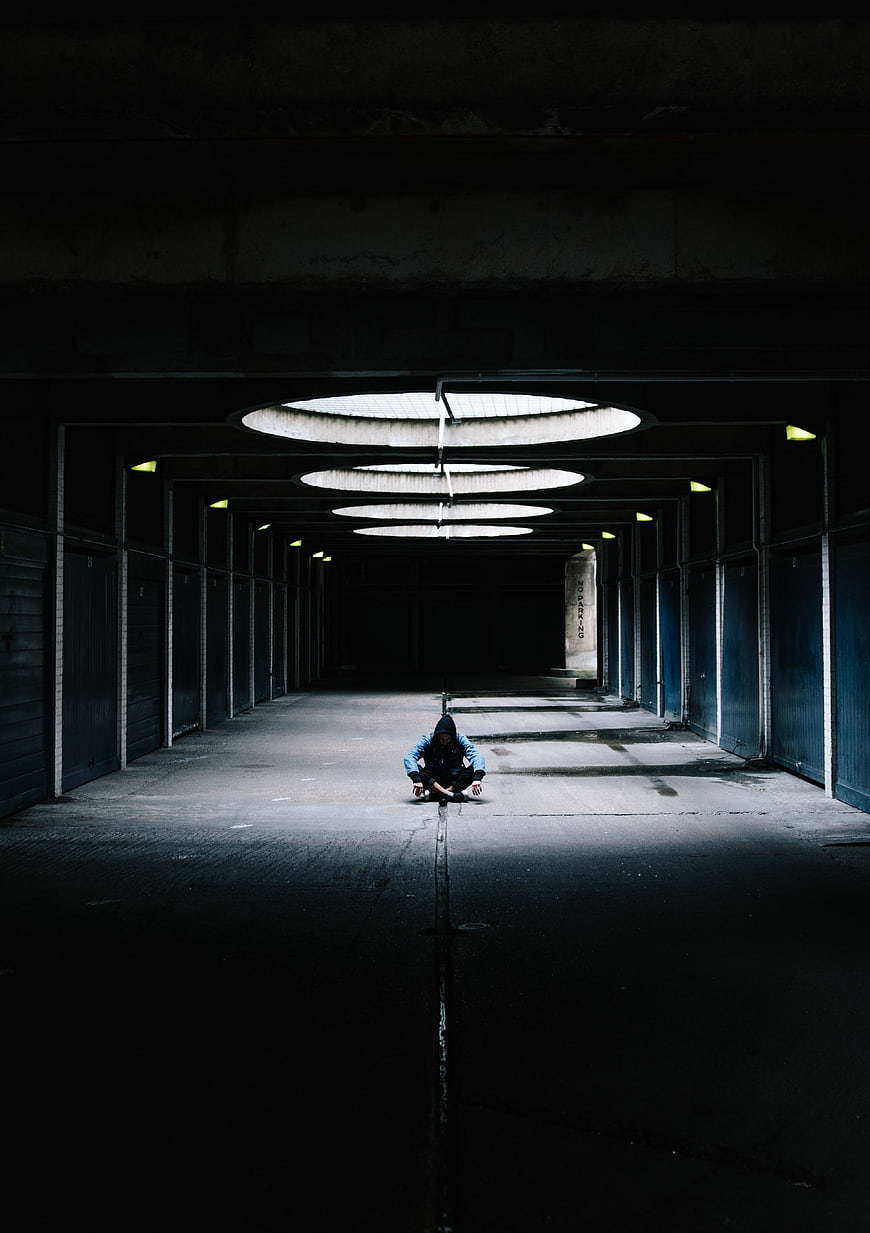 Man sitting alone in dark industrial corridor with overhead lights