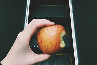 Hand holding bitten apple on escalator