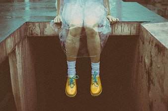 Girl in yellow rain boots sitting on concrete ledge
