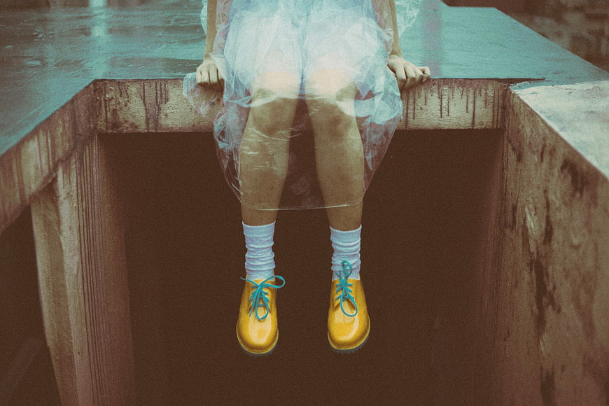 Girl in yellow rain boots sitting on concrete ledge