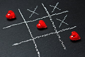 Red heart candies winning tic tac toe game on black chalkboard