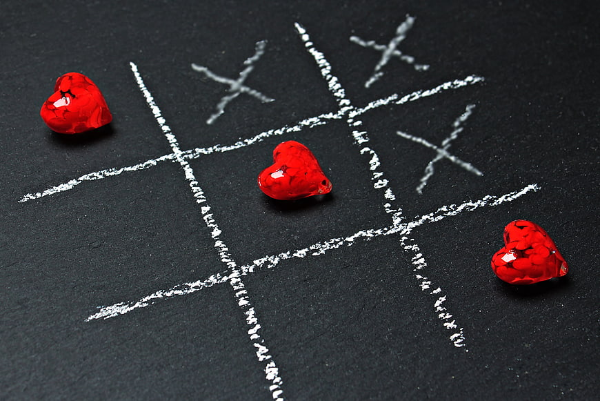 Red heart candies winning tic tac toe game on black chalkboard