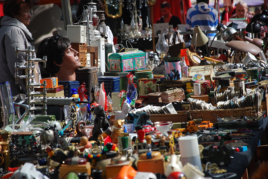 Woman Browsing Cluttered Antiques Table At Outdoor Flea Market