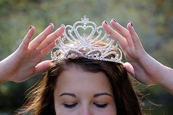Woman placing jeweled tiara on head outdoors