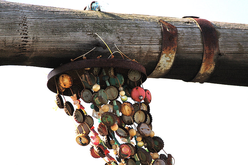 Rustic DIY wind chime made of bottle caps hanging from a weathered wooden pole