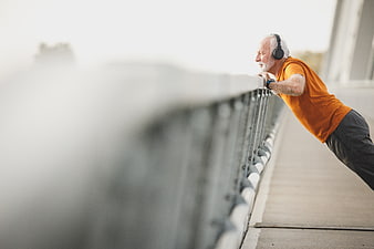 Senior man doing pushups on bridge railing with headphones