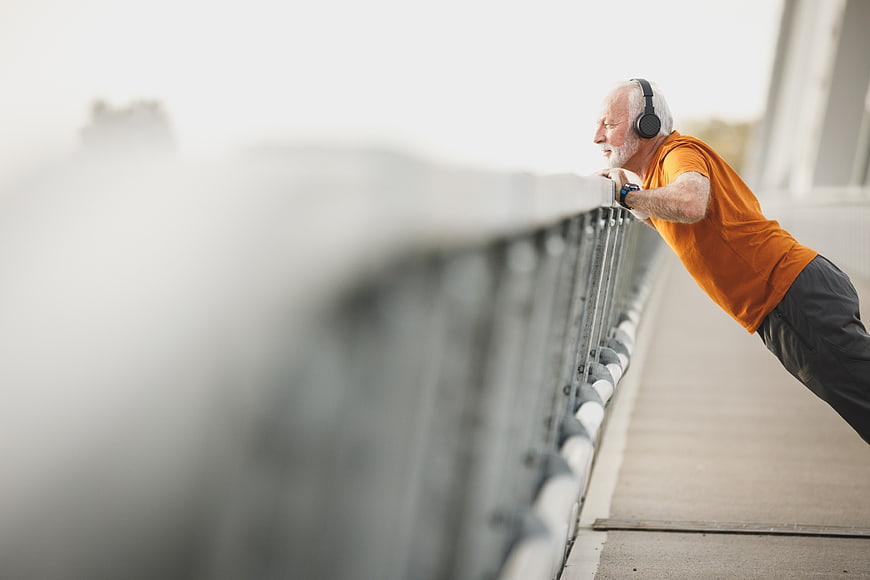 Senior man doing pushups on bridge railing with headphones