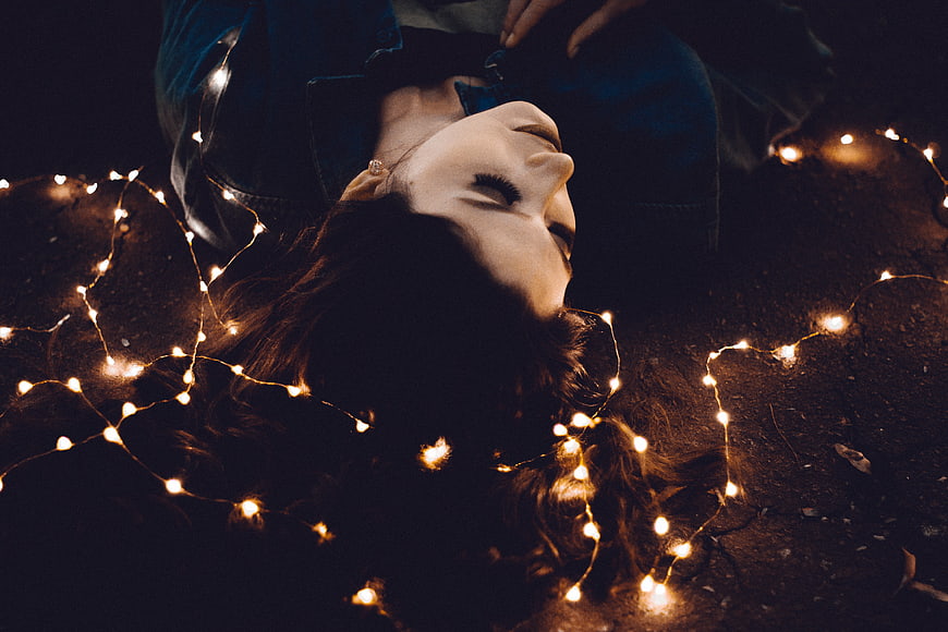 Woman lying down surrounded by warm fairy lights at night