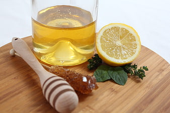 Glass Jar of Honey with Lemon, Mint, and Wooden Dipper on Wooden Board