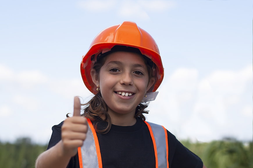 Smiling child in orange hard hat giving thumbs up