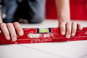 Close-up of hands using a red spirit level on white tiles