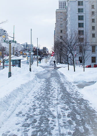 Snowy urban sidewalk with footprints and city buildings