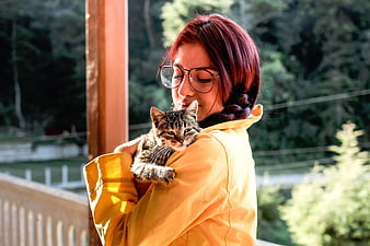 Woman with red hair holding tabby cat on wooden porch