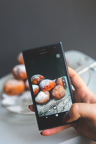 Hand holding smartphone photographing powdered donuts