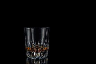 Glass of amber whiskey on black background