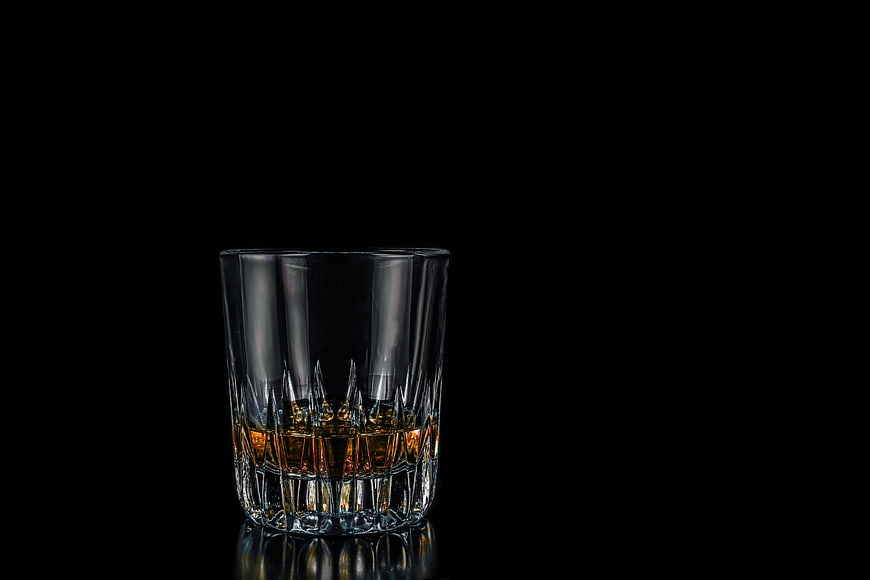 Glass of amber whiskey on black background