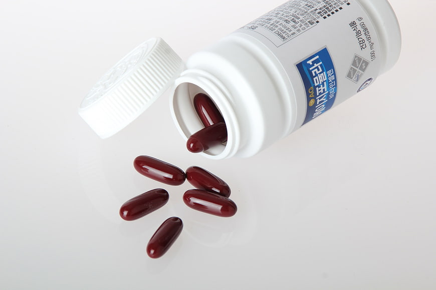 White supplement bottle with dark red capsules spilling on white background