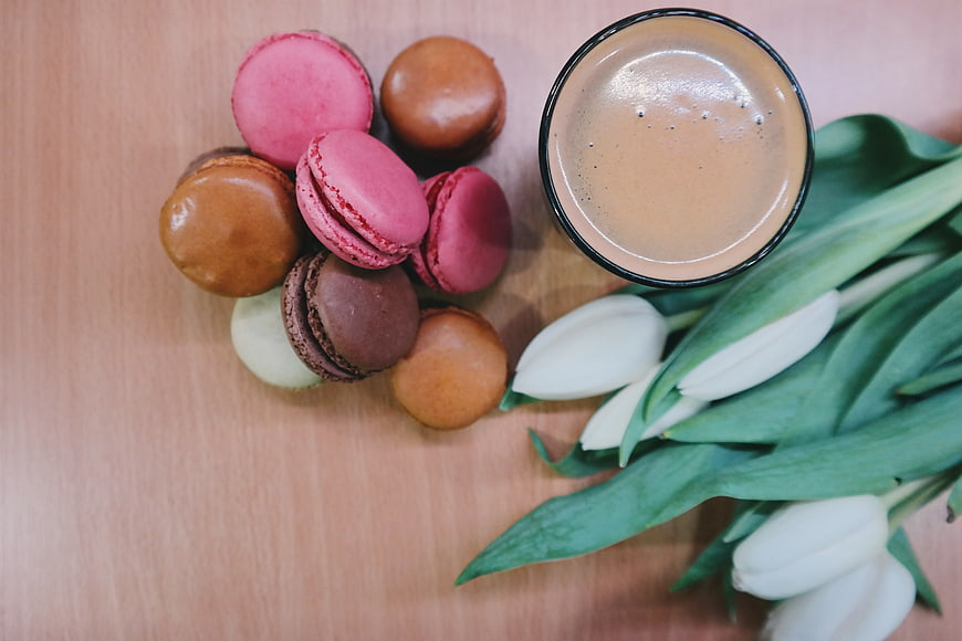 Flat lay of colorful macarons, coffee, and white tulips on wood