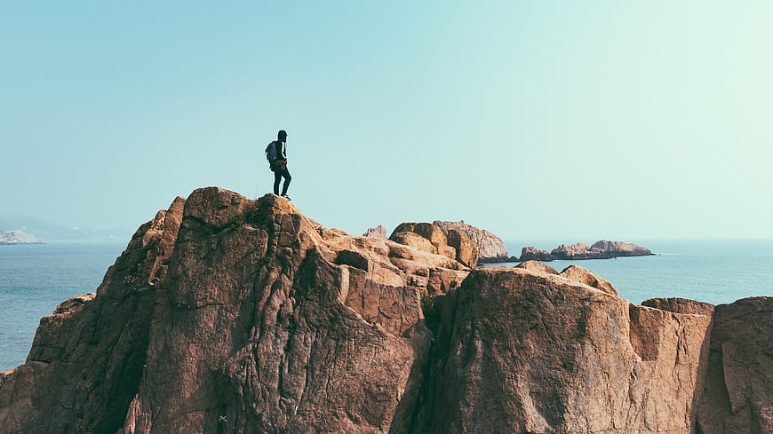 Hiker standing on rocky cliff overlooking the ocean