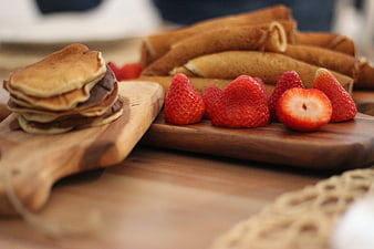 Stack of mini pancakes with chocolate and fresh strawberries on wooden board