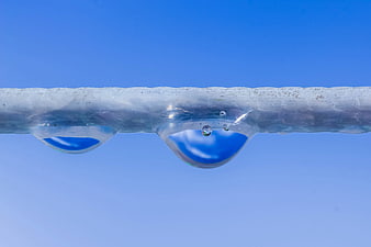 Macro shot of water droplets dripping from ice against blue sky