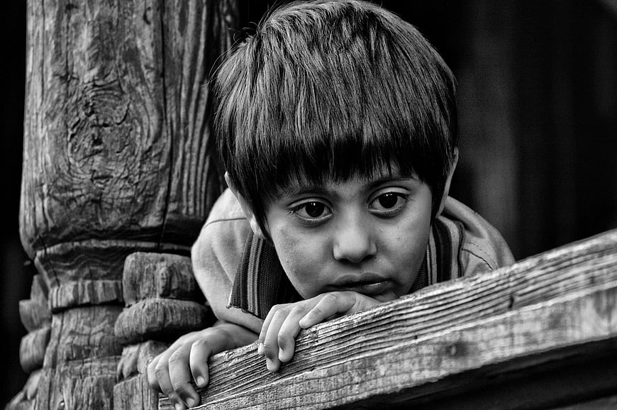 Black and white portrait of a young boy looking over a wooden railing