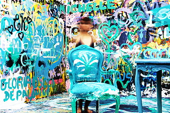 Woman sitting on turquoise chair in front of colorful graffiti wall