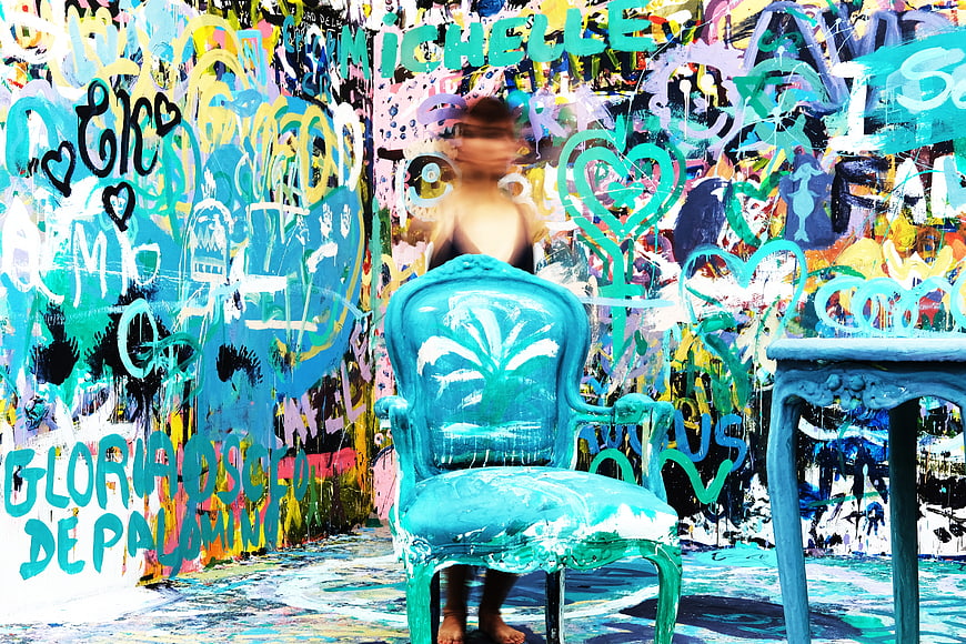 Woman sitting on turquoise chair in front of colorful graffiti wall