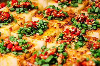 Close-up of Sichuan tofu topped with chopped green onions and red chili peppers