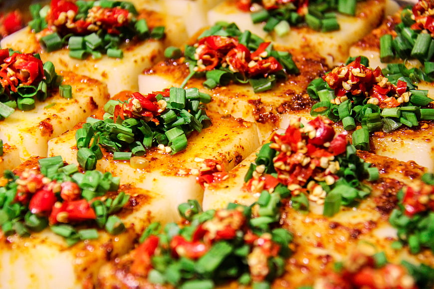 Close-up of Sichuan tofu topped with chopped green onions and red chili peppers
