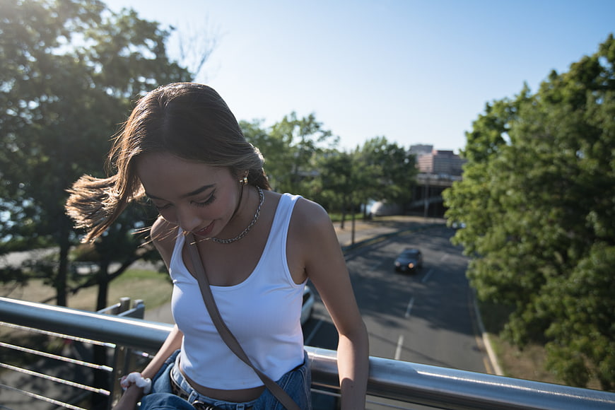Young woman in white tank top sitting on bridge railing