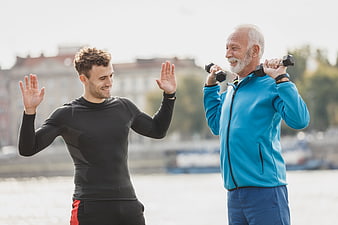 Senior man lifting dumbbells with personal trainer outdoors