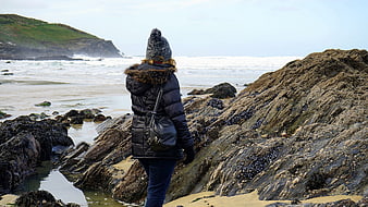 Woman in Winter Coat Exploring Rocky Coastal Beach