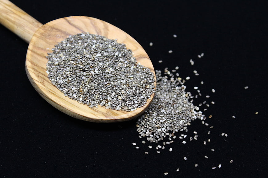 Chia seeds in wooden spoon on black background