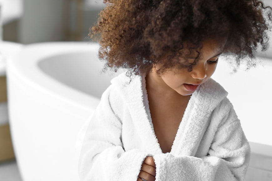Cute child in white bathrobe looking down in bathroom