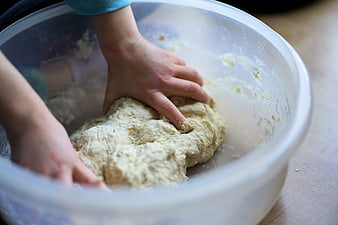 Child kneading yeast dough in a clear plastic mixing bowl