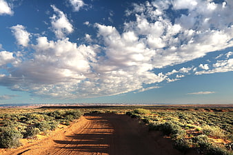 Dirt Road Through Desert Landscape Under Blue Sky with Clouds