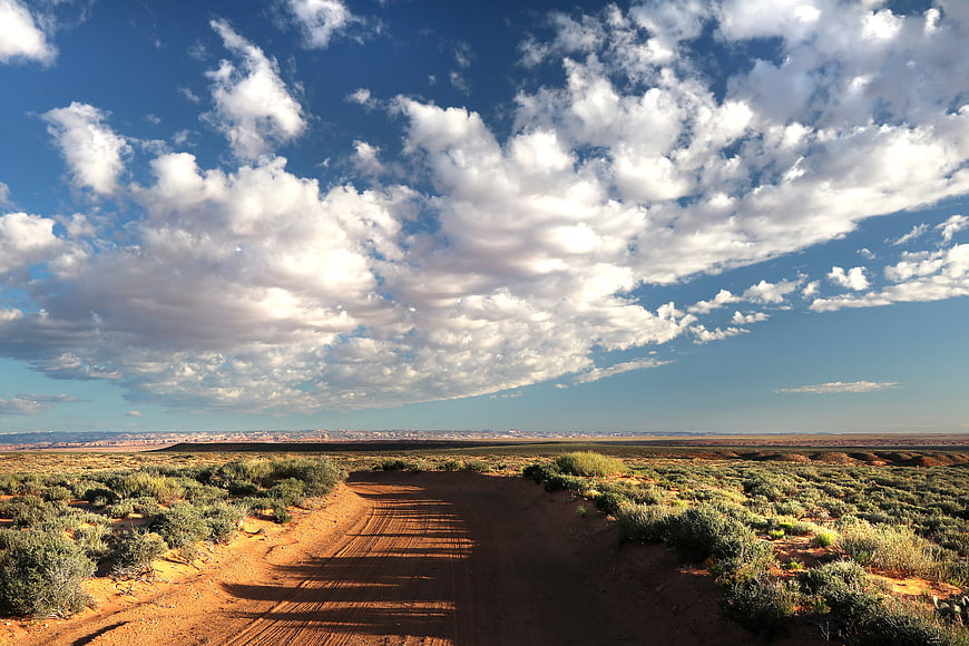 Dirt Road Through Desert Landscape Under Blue Sky with Clouds