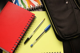 Red Notebook and Pens on Yellow Paper with Black Bag