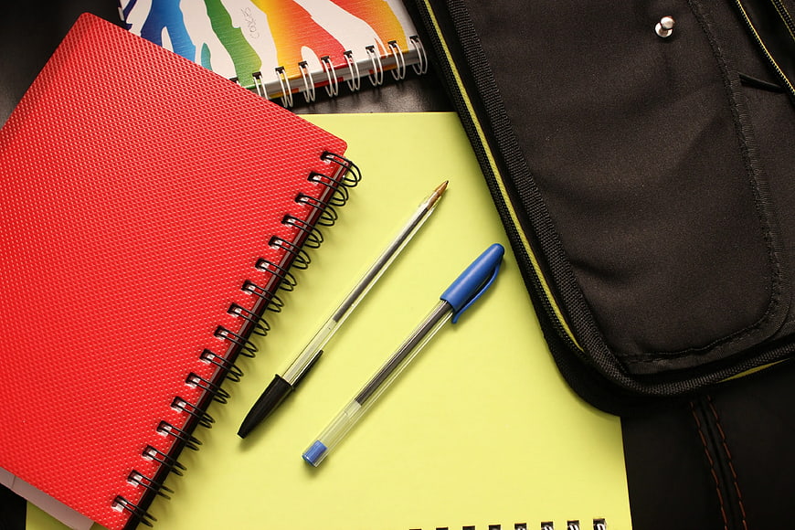 Red Notebook and Pens on Yellow Paper with Black Bag