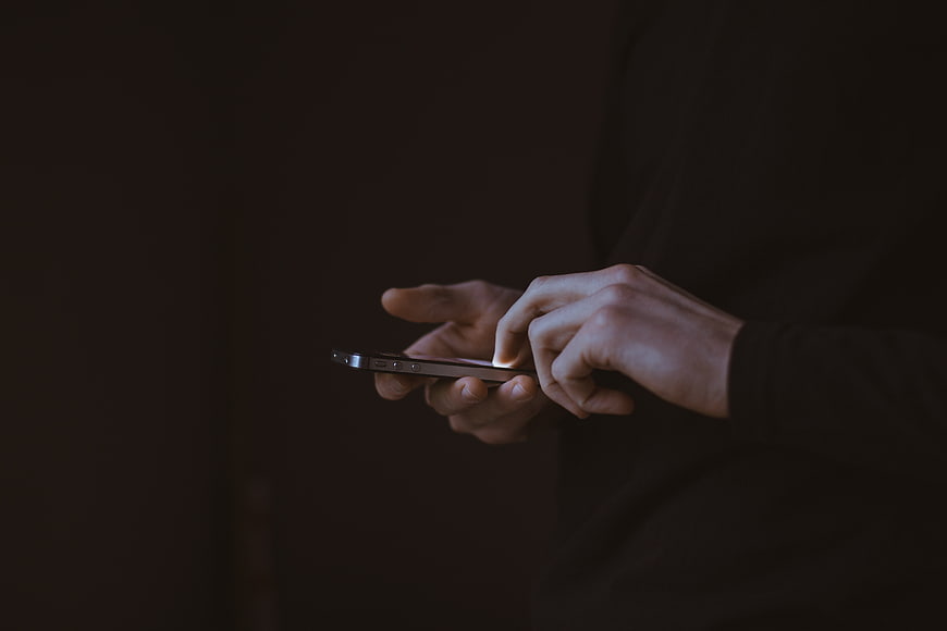Close-up of hands typing on smartphone in dark setting