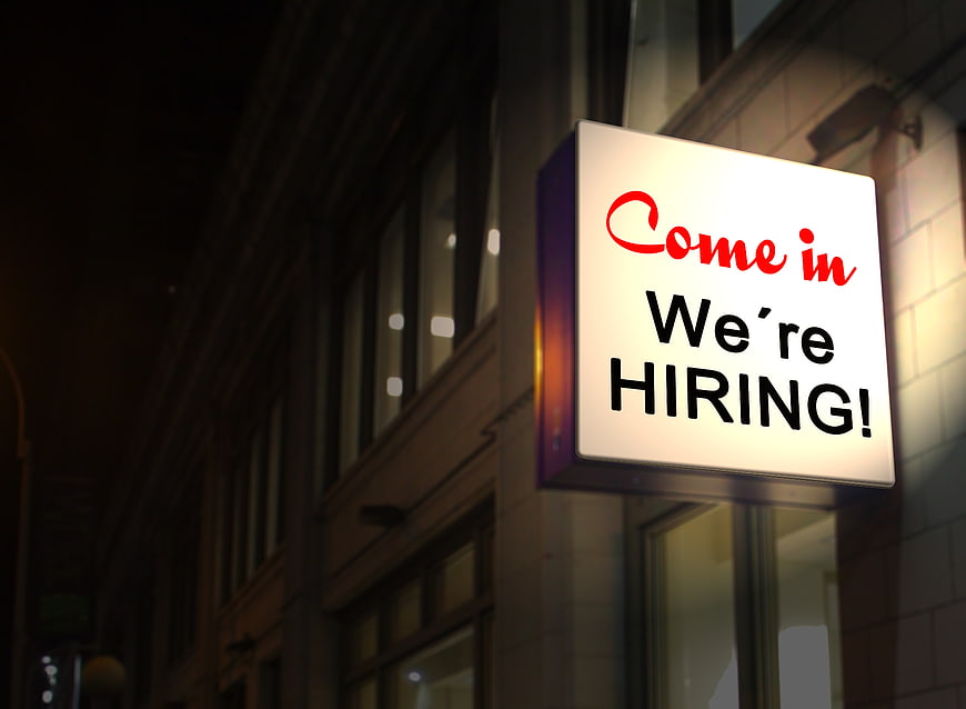 Illuminated We're Hiring Sign on Building at Night