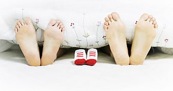 Pregnant Couple Feet Under Quilt With Baby Socks