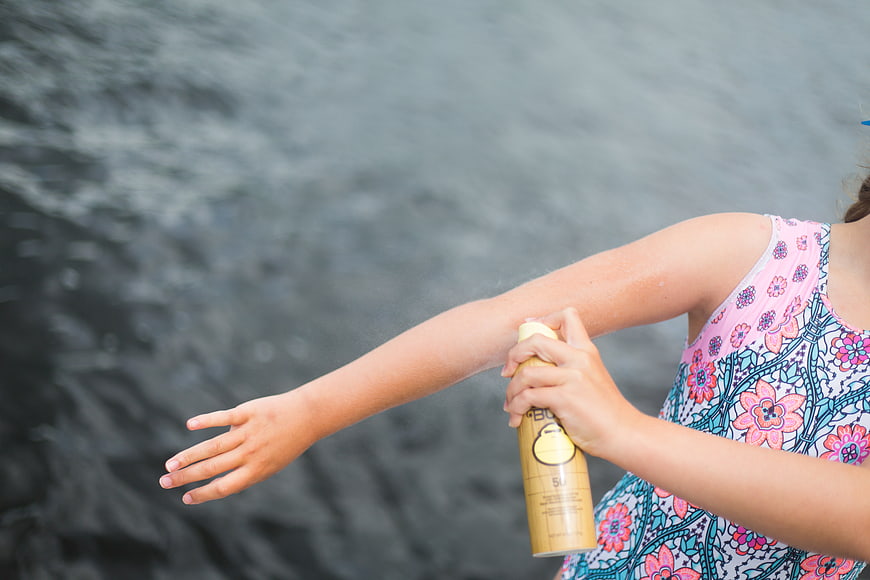 Girl applying sunscreen spray at the lake
