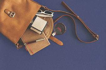 Flat lay of brown leather handbag with accessories on blue background