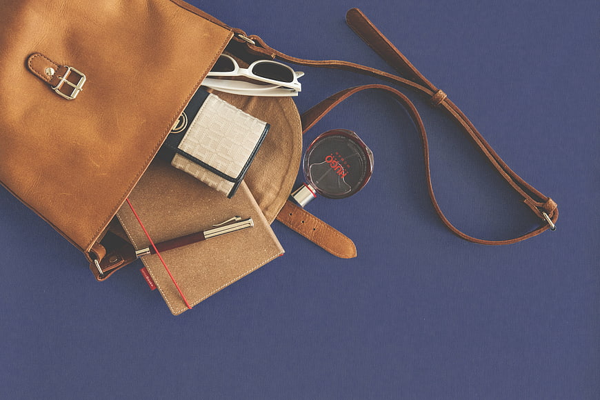 Flat lay of brown leather handbag with accessories on blue background